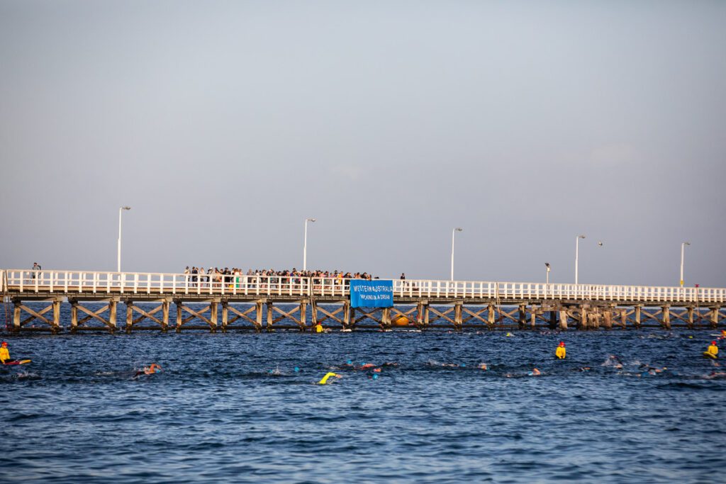 People swimming along the Jetty. A crowd is cheering them on from the Jetty