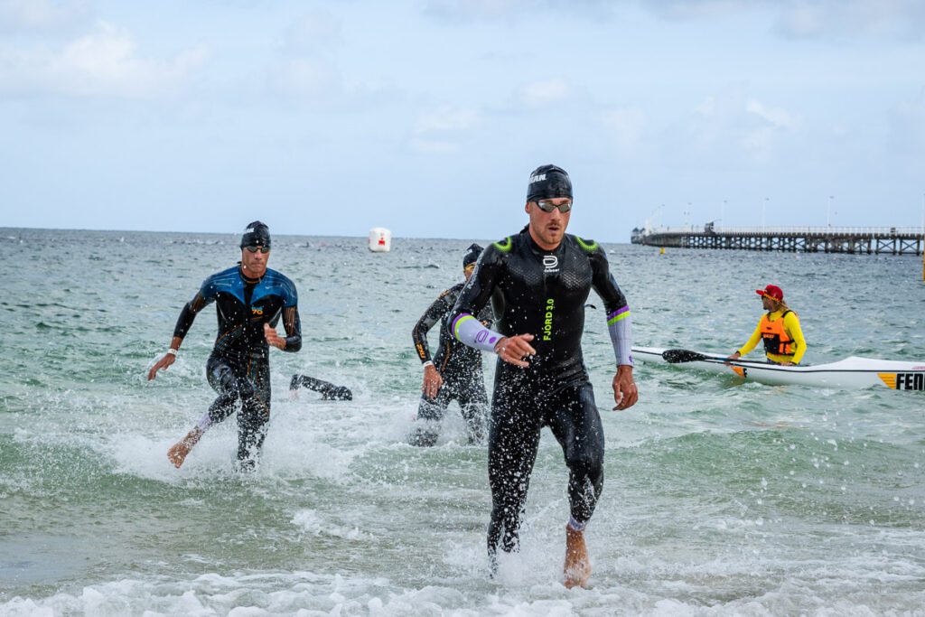 Iron Man swimmers running up the beach after swimming around the Jetty