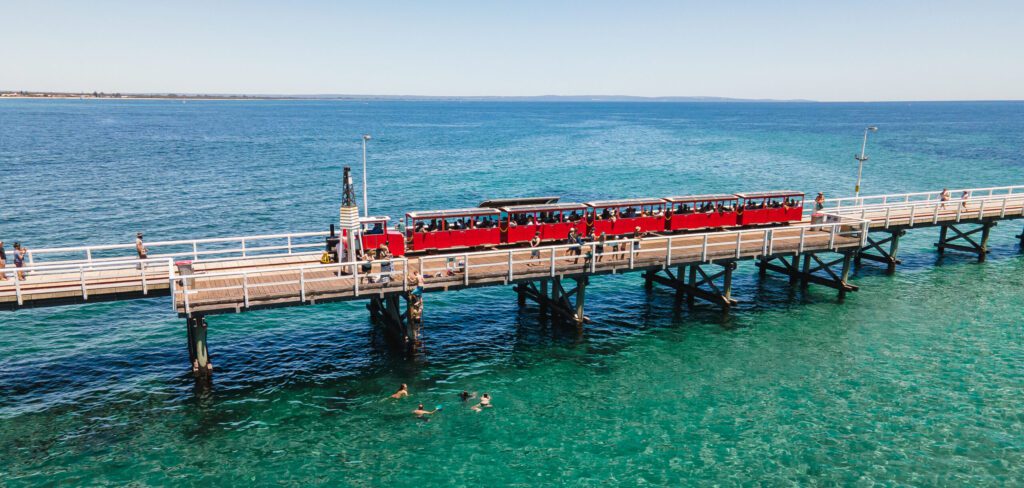 The bright-red Busselton Jetty Train travelling above the crystal clear waters of Geographe Bay