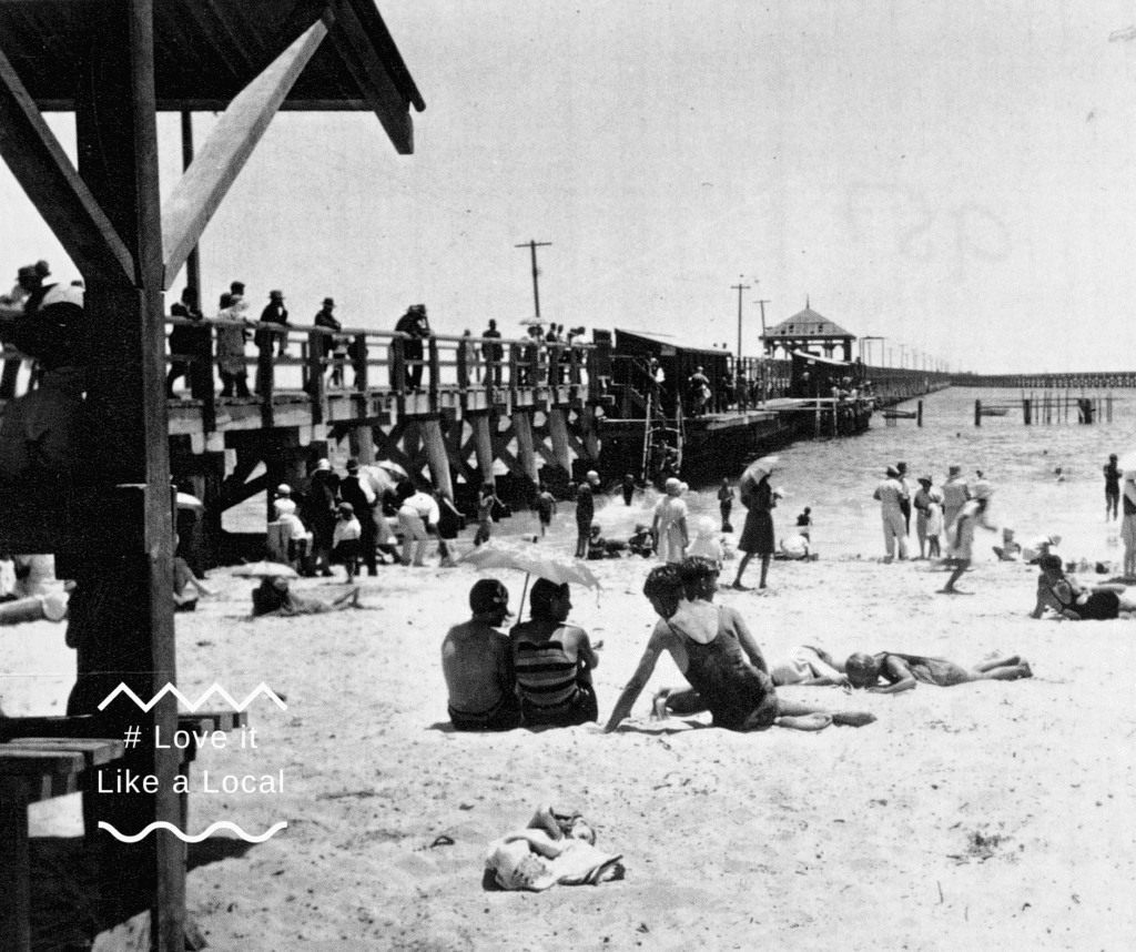 Old black-and-white photo of people on the beach and jetty