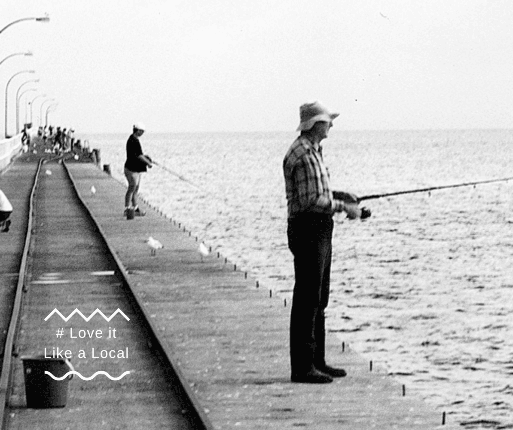 Old black-and-white photo of a man fishing off the jetty